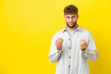Sarı arka planda soyutlanmış yakışıklı beyaz bir adam para jesti yapıyor ama mahvoluyor.