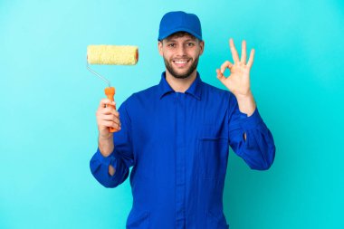Boyacı beyaz adam mavi arka planda izole edilmiş. Parmaklarıyla tamam işareti gösteriyor.