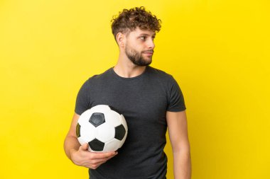 Sarı arka planda izole edilmiş yakışıklı genç futbolcu yan tarafa bakıyor.