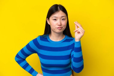 Sarı arka planda izole edilmiş genç Çinli kadın İtalyan jestleri yapıyor.