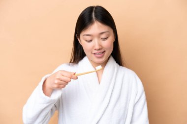 Genç Çinli kadın bej arka planda izole edilmiş diş fırçası ve mutlu bir ifadeyle.