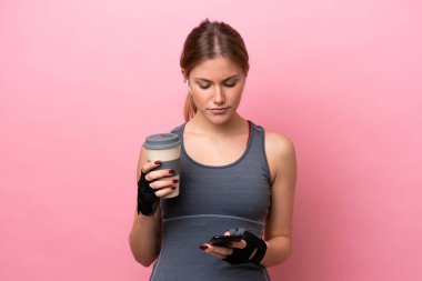Pembe arka planda izole edilmiş beyaz bir kadın elinde kahve ve cep telefonu ile geziyor.