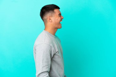 Soyutlanmış mavi arka planda genç yakışıklı adam yan yana gülüyor.