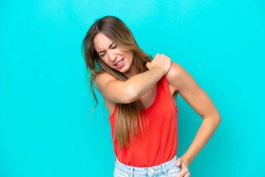 Genç, beyaz bir kadın mavi arka planda izole edilmiş. Omuz ağrısı çekiyor. Çabaladığı için.