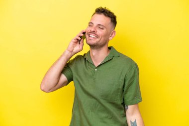 Sarı arka planda izole genç beyaz yakışıklı adam cep telefonuyla sohbet ediyor.