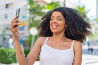 Genç Afrikalı Amerikalı bir kadın açık havada selfie çekiyor.