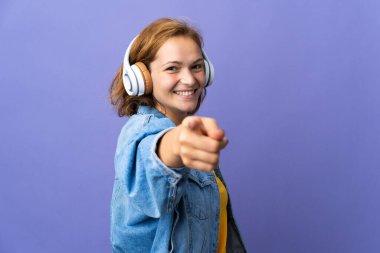 Genç Gürcü kadın mor arka planda izole edilmiş müzik dinliyor ve ön tarafı işaret ediyor.