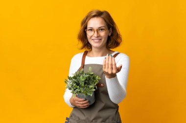 Sarı arka planda izole edilmiş bir bitkiyi tutan genç Gürcü kadın bizimle gelmesi için davet ediyor. Gelmene sevindim.