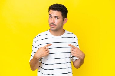 Soyutlanmış sarı arka planı olan yakışıklı genç bir adam kendini işaret ediyor.