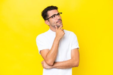 Soyutlanmış sarı arka planı olan yakışıklı bir genç. Şüpheleri var.