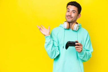Genç yakışıklı bir adam, izole bir duvarın üzerinde bilgisayar oyunu kontrolörüyle oynuyor. Davet etmek için ellerini yana açıyor.