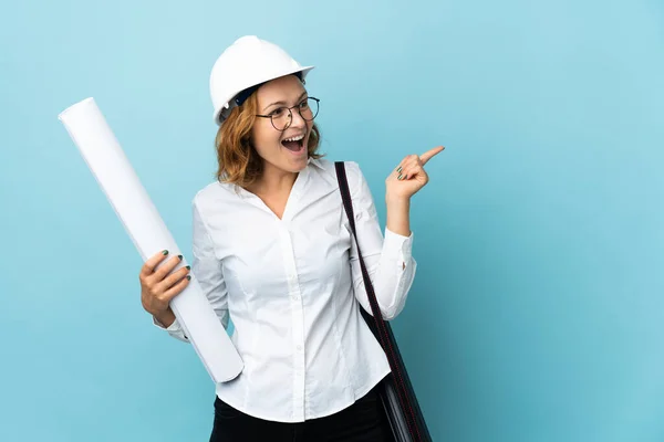 Young architect Georgian woman with helmet and holding blueprints over isolated background intending to realizes the solution while lifting a finger up