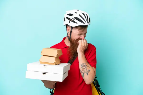 Delivery man holding pizzas and burgers isolated on blue background having doubts