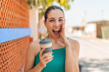 Genç ve güzel bir kadın açık havada kahve alıp, ağzı açık bağırıyor.