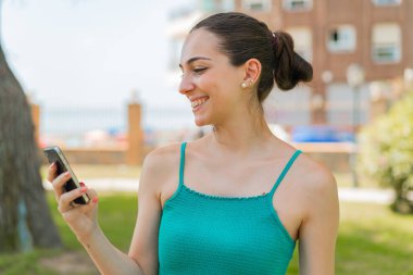 Açık havada cep telefonu kullanan genç ve güzel bir kadın.