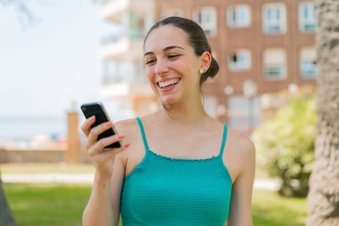 Açık havada cep telefonu kullanan genç ve güzel bir kadın.