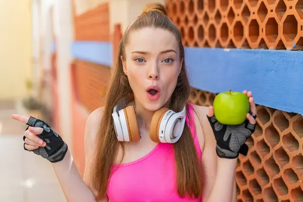 Açık havada elmalı genç ve güzel bir kız şaşırmış ve işaret ediyor.