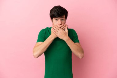 Pembe arka planda izole edilmiş genç bir Rus adam elleriyle ağzını kapatıyor.
