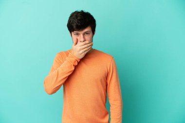 Genç Rus adam mavi arka planda tek başına ağzını eliyle kapatıyor.