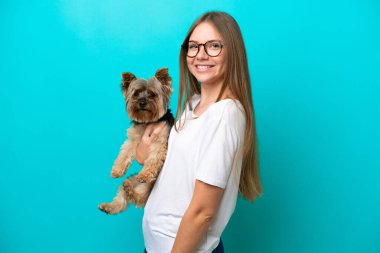 Genç Litvanyalı bir kadın mavi arka planda izole edilmiş bir köpeği tutarken çok gülümsüyor.