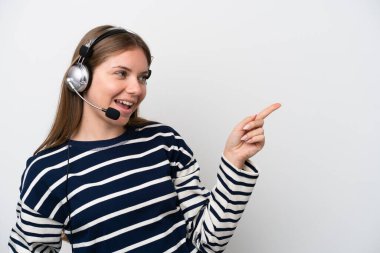 Beyaz arka planda izole edilmiş bir kulaklıkla çalışan beyaz pazarlamacı kadın, parmağını yana uzattı ve bir ürün sundu.