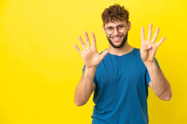 Sarı arka planda izole edilmiş yakışıklı beyaz adam dokuz parmaklı sayıyor.