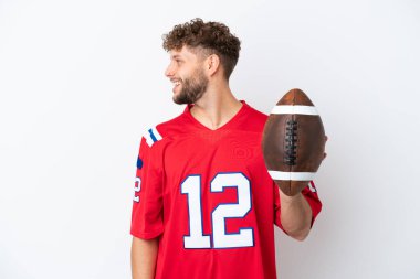 Beyaz arka planda ragbi oynayan beyaz tenli genç adam yan pozisyonda gülüyor.