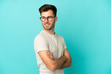 Beyaz tenli yakışıklı adam mavi arka planda izole edilmiş, yana bakıyor ve gülümsüyor.