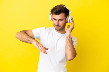 Beyaz tenli yakışıklı adam sarı arka planda izole edilmiş müzik ve dans dinliyor.