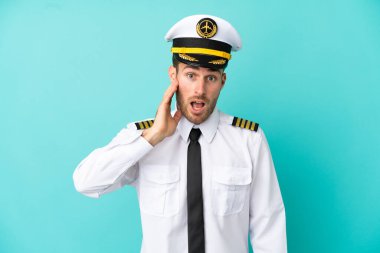 Kafkasyalı uçak pilotu mavi arka planda şaşırmış ve şok olmuş bir yüz ifadesiyle izole edilmiş.