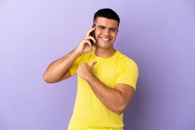 İzole edilmiş mor arka planda cep telefonu kullanan yakışıklı genç adam gururlu ve kendini beğenmiş.