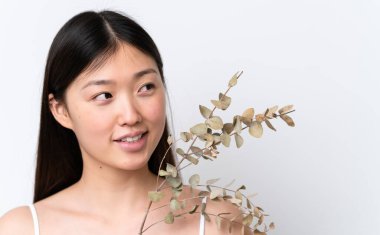 Young Chinese woman isolated on white background holding a eucalyptus branch while smiling. Close up portrait