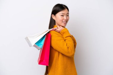 Beyaz arka planda izole edilmiş genç bir Çinli kadın alışveriş torbaları tutuyor ve gülümsüyor.