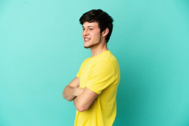 Genç Rus adam mavi arka planda izole edilmiş kolları bağlı ve mutlu.