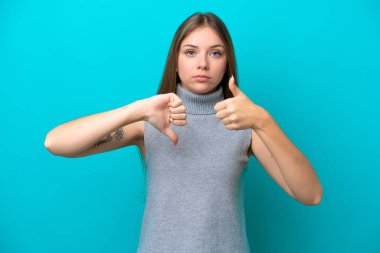 Genç Litvanyalı kadın mavi arka planda izole edilmiş, iyiye kötüye işaret yapıyor. Evet ya da hayır arasında kararsız