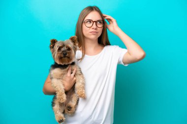 Genç Litvanyalı bir kadın mavi arka planda izole edilmiş bir köpek tutuyor. Şüpheleri var ve kafası karışmış bir yüz ifadesi var.