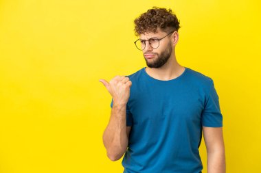 Sarı arka planda izole edilmiş yakışıklı beyaz adam mutsuzdu ve yüzünü gösteriyordu.