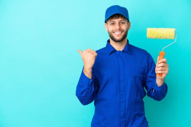 Kafkasyalı ressam, mavi arka planda izole edilmiş bir şekilde bir ürün sunmak için kenarı işaret ediyor.