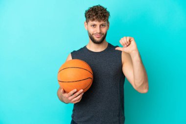 Basketbol oynayan yakışıklı genç adam mavi arka planda soyutlanmış gururlu ve kendinden memnun.