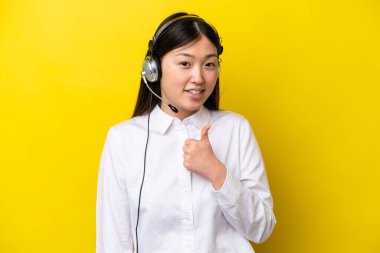 Tele pazarlamacı Çinli kadın sarı arka planda izole edilmiş bir kulaklıkla çalışıyor.