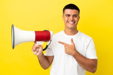 Soyutlanmış sarı arka planda genç yakışıklı bir adam elinde megafon ve işaret eden bir taraf tutuyor.
