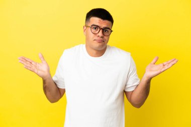 El kaldırırken şüpheleri olan izole sarı arka plan üzerinde genç yakışıklı adam