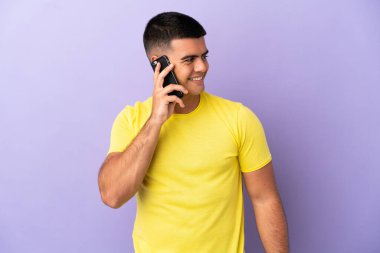 İzole edilmiş mor arka plan üzerinde cep telefonu kullanan genç yakışıklı bir adam.