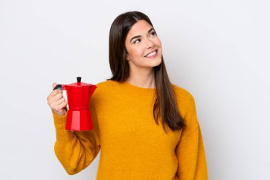 Beyaz arka planda kahve demliği tutan Brezilyalı genç bir kadın gülümserken yukarı bakıyor.