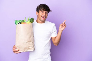 Elinde mor arka planda izole edilmiş bir alışveriş poşeti tutan genç adam çözümü bulmak için parmağını kaldırıyor.