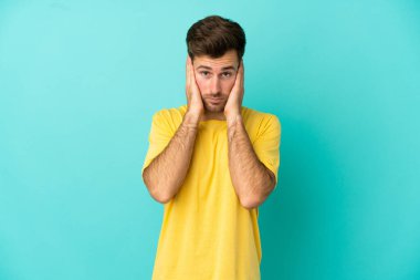 Kafkasyalı yakışıklı adam mavi arka planda izole edilmiş hayal kırıklığına uğramış ve kulaklarını kapatmış.
