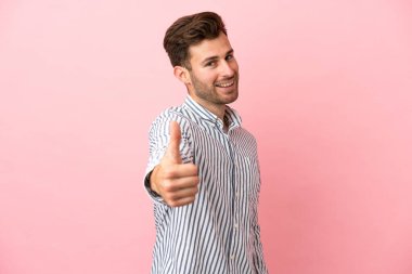 Beyaz tenli yakışıklı bir adam pembe arka planda izole edilmiş. Başparmakları havada. Çünkü iyi bir şey oldu.