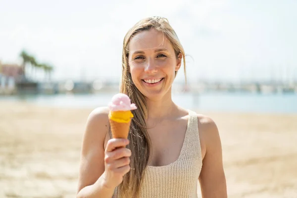 Young blonde woman with a cornet ice cream at outdoors smiling a lot