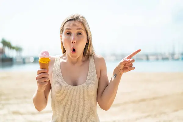 Young blonde woman with a cornet ice cream at outdoors surprised and pointing side