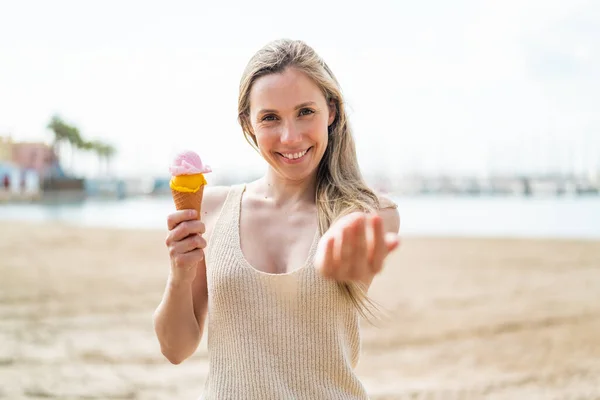 若い金髪の女性は 屋外でコルネットアイスクリームを持ち 手で来ることを勧めます 来てくれてうれしい — ストック写真